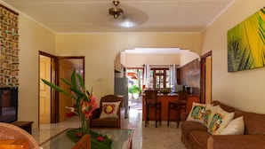 A living room with a sofa, armchairs, a coffee table, a TV, and a decorative plant. - Villas des Alizes (Praslin Island)