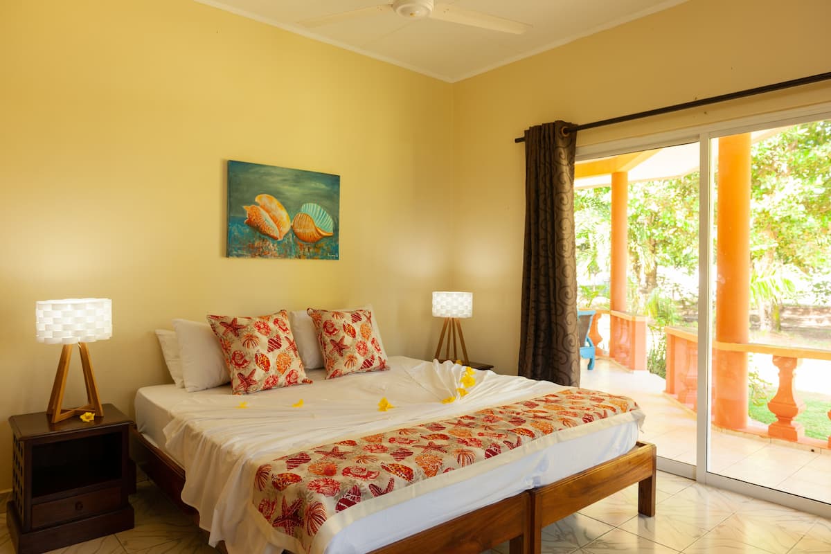 A hotel room with a bed, two bedside tables, a painting, and a view of the outdoors.