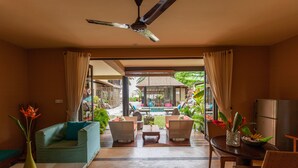 A room with a sofa, a dining table, and chairs, a ceiling fan, and a view of an outdoor pool area. - Villas des Alizes (Praslin Island)