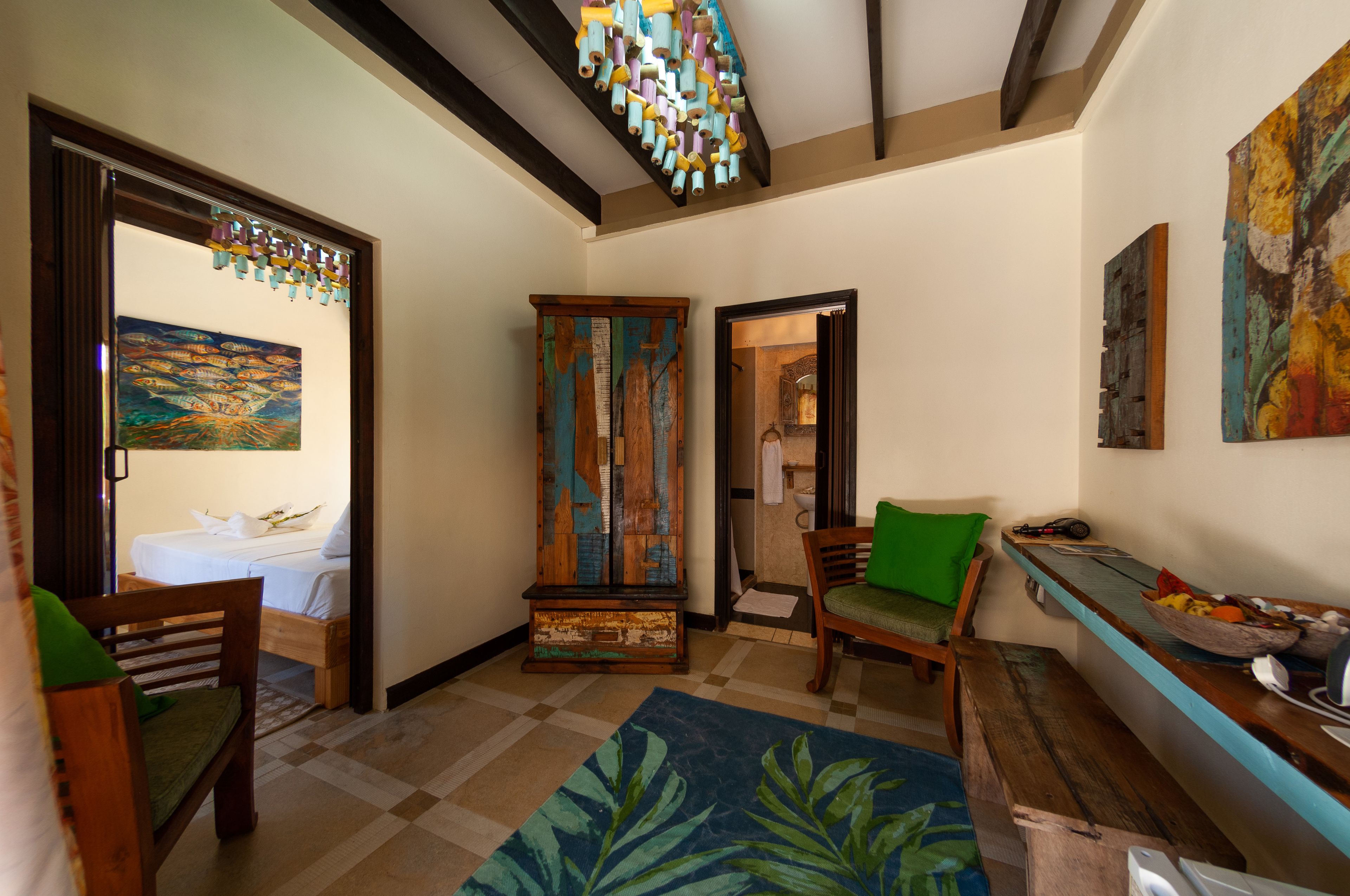 Una habitación de hotel con una cama, un armario de madera, una silla verde, un banco y una pared con un cuadro.