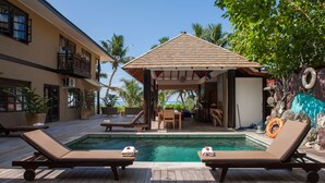 A pool area with lounge chairs, a covered seating area, and a view of the ocean. - Villas des Alizes (Praslin Island)