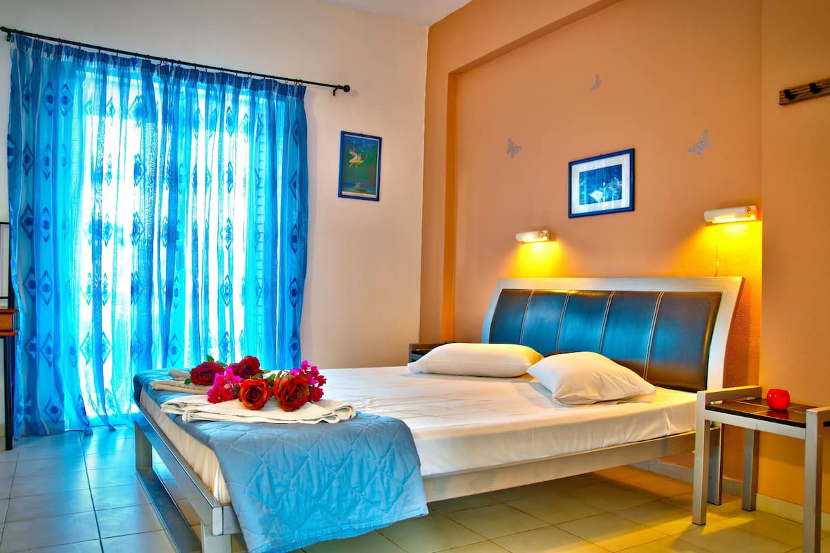 A hotel room with a bed, a bedside table, a nightstand, and a window with curtains.