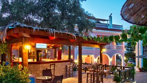 An outdoor bar area with stone flooring, wooden furniture, and a thatched roof. - Kyprianos (Zakynthos)