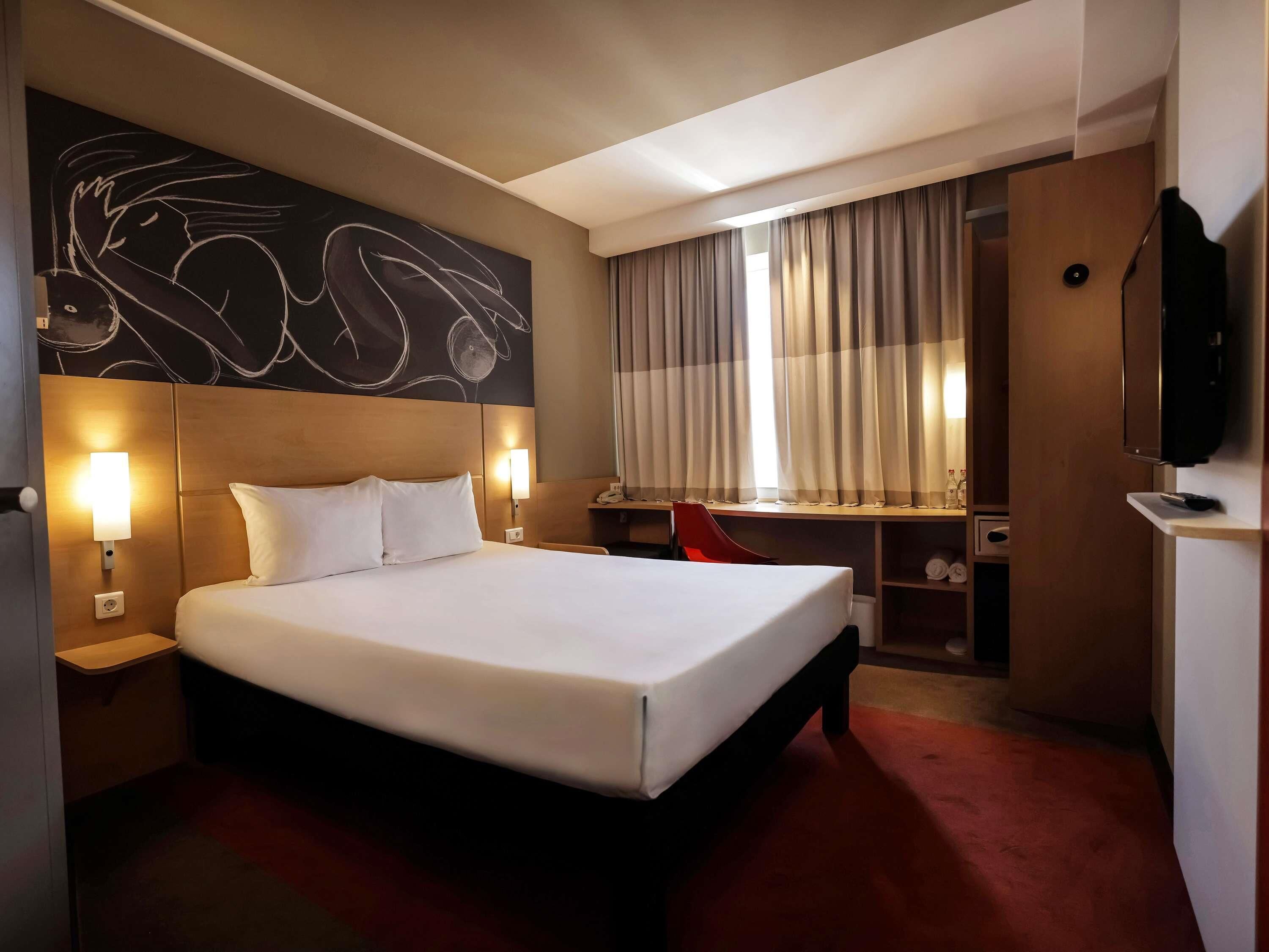 Habitación de hotel con una cama grande, un escritorio, una silla, televisión y una pared con arte abstracto.