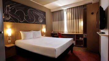 Habitación de hotel con una cama grande, un escritorio, una silla, televisión y una pared con arte abstracto.