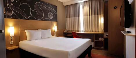 A hotel room with a large bed, a desk, a chair, a television, and a wall with abstract art.