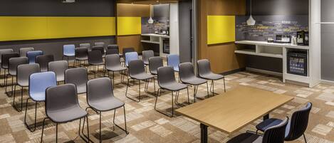 Un salón de conferencias con una amplia mesa y múltiples sillas, una zona de kitchenette y una pared con citas inspiradoras.