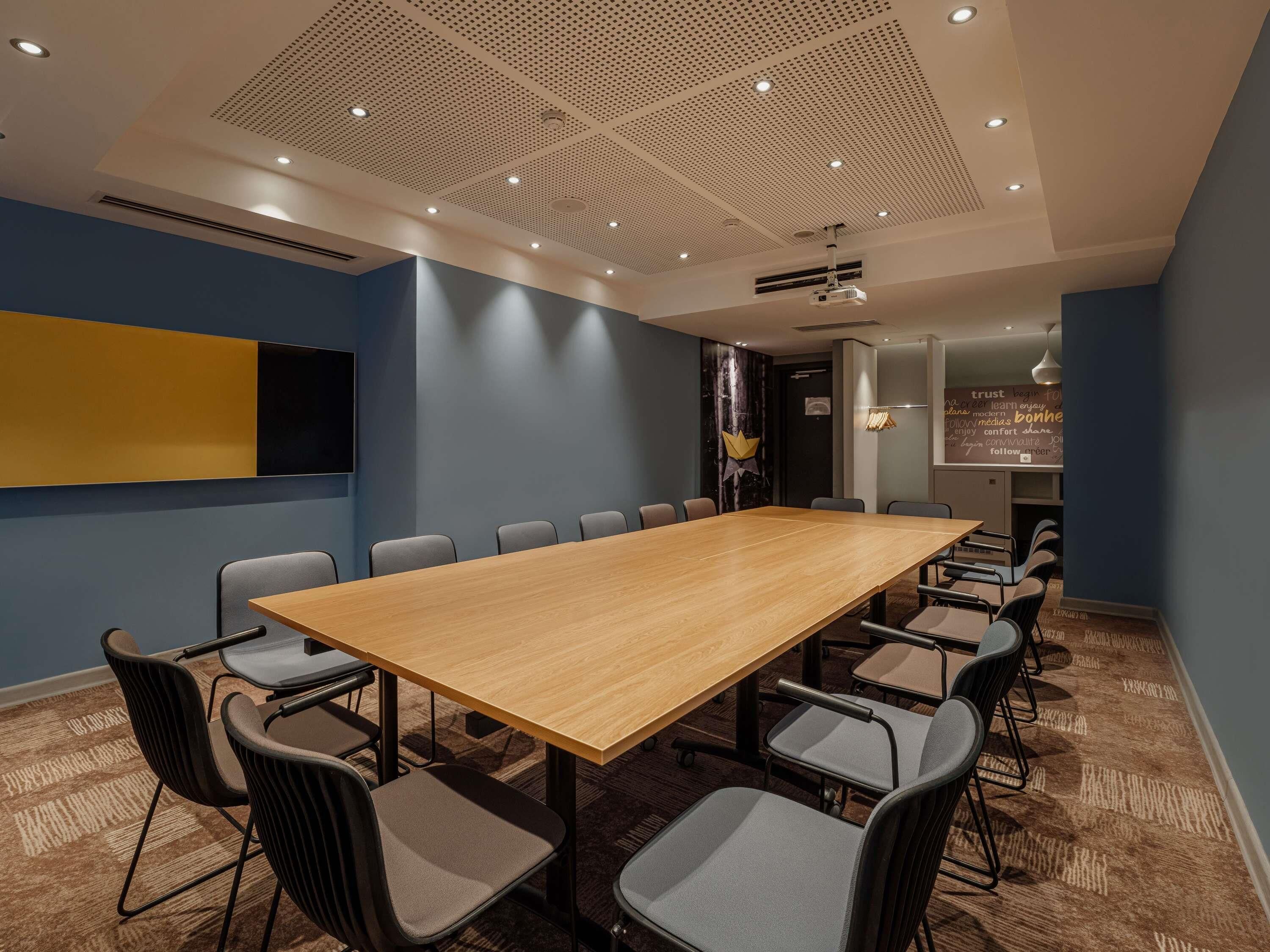 Une salle de conférence équipée d’une longue table, de chaises, d’un projecteur et d’un écran fixé au mur.