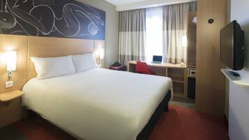 A hotel room with a large bed, a desk with a laptop, a television, and a wall art piece.
