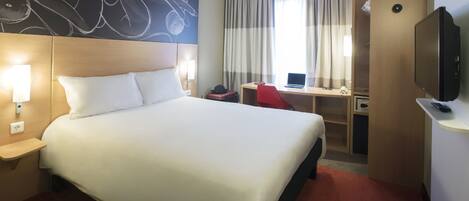 A hotel room with a large bed, a desk with a laptop, a television, and a wall art piece.