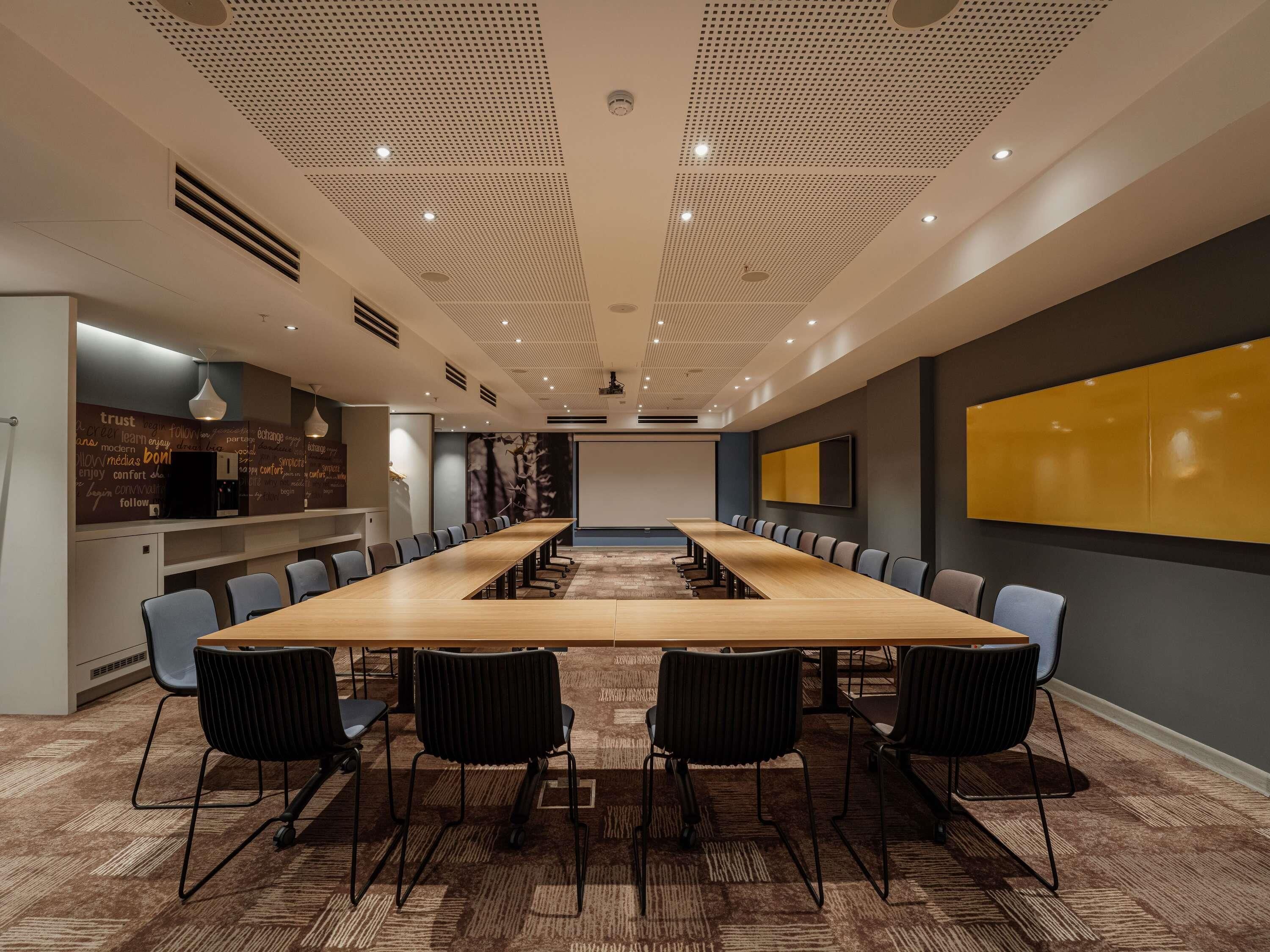 A conference room with a long table, chairs, a projector screen, and a wall with motivational words.