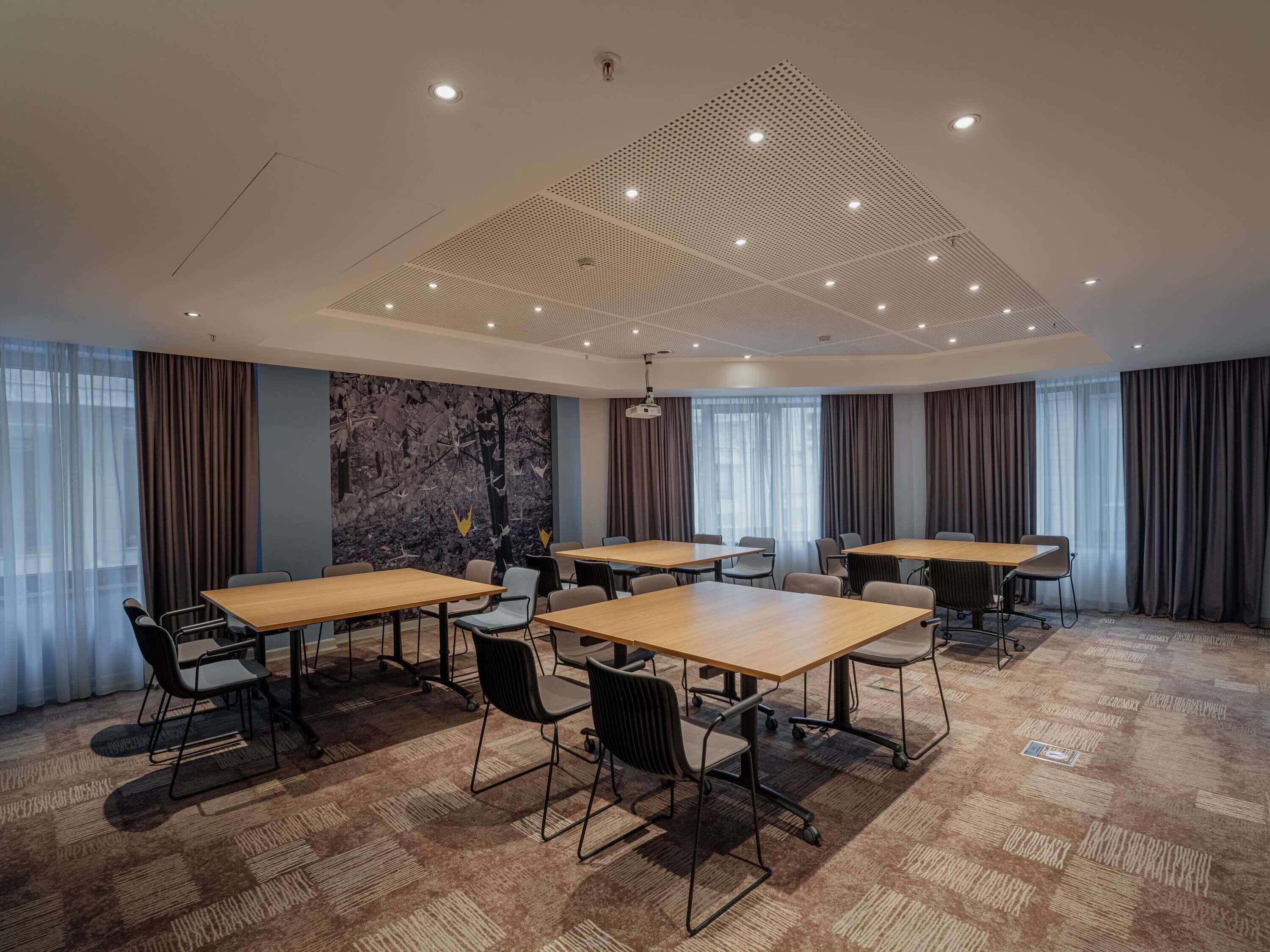 A conference room with a modern ceiling design, large windows with curtains, and a carpeted floor.