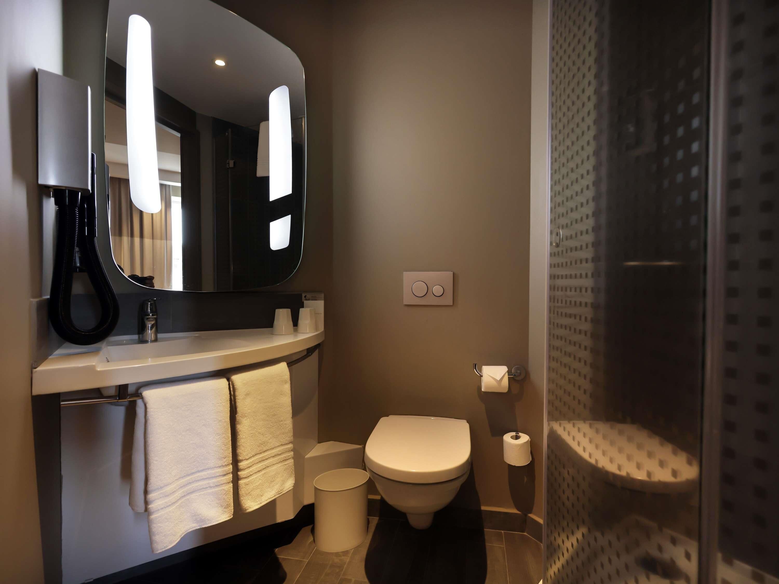 A modern bathroom with a sink, mirror, towel rack, toilet, and a shower area.
