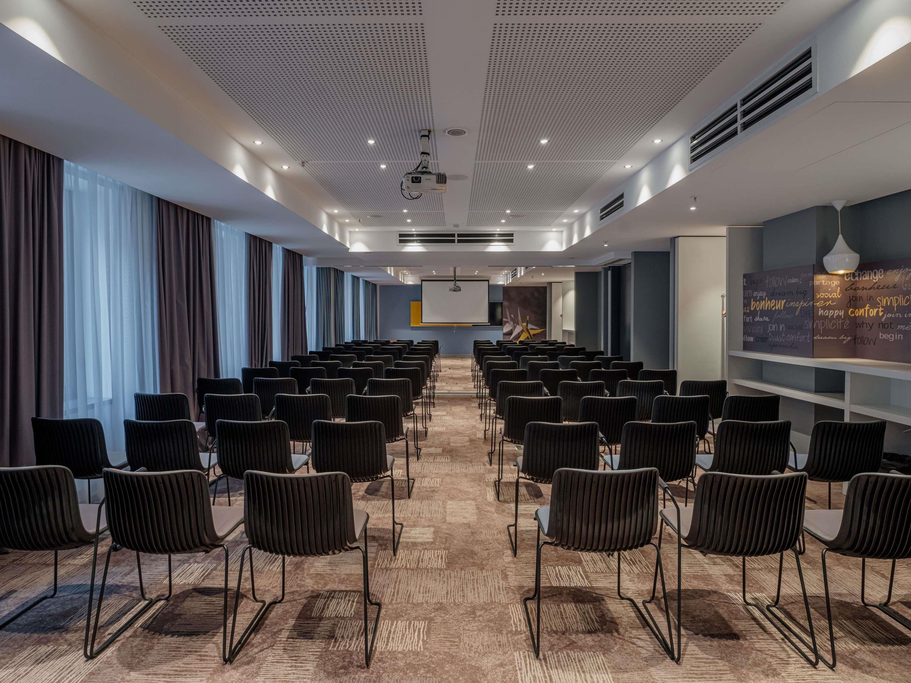 A conference room with rows of chairs, a projector, and a presentation screen.