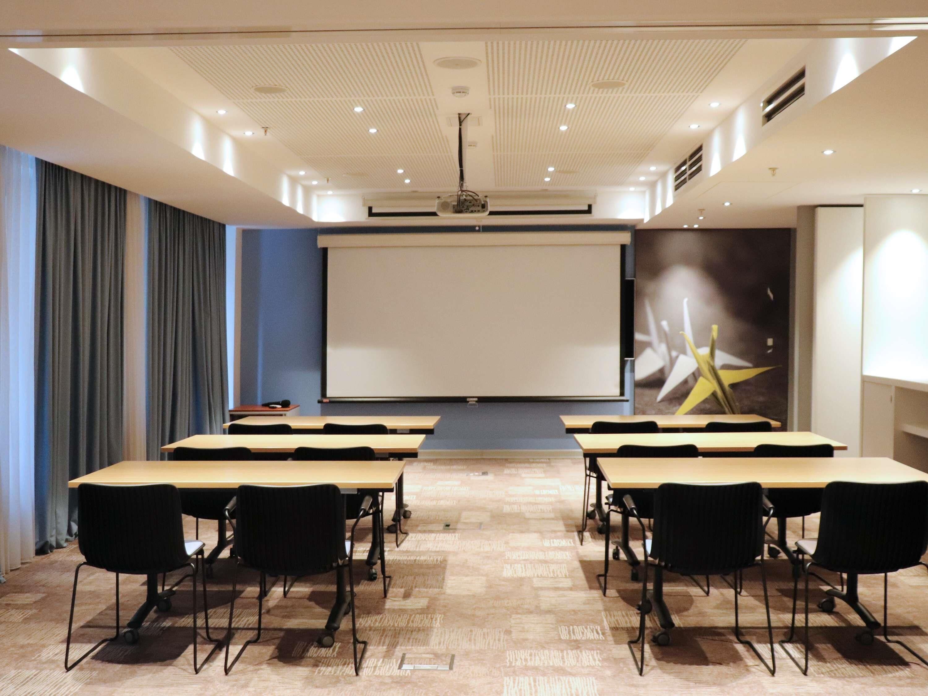 A conference room with a large screen, tables, and chairs arranged for presentations.