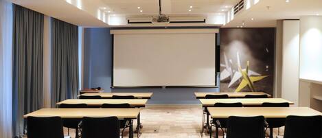 Une salle de conférence équipée d’un grand écran, de tables et de chaises disposées pour les présentations.