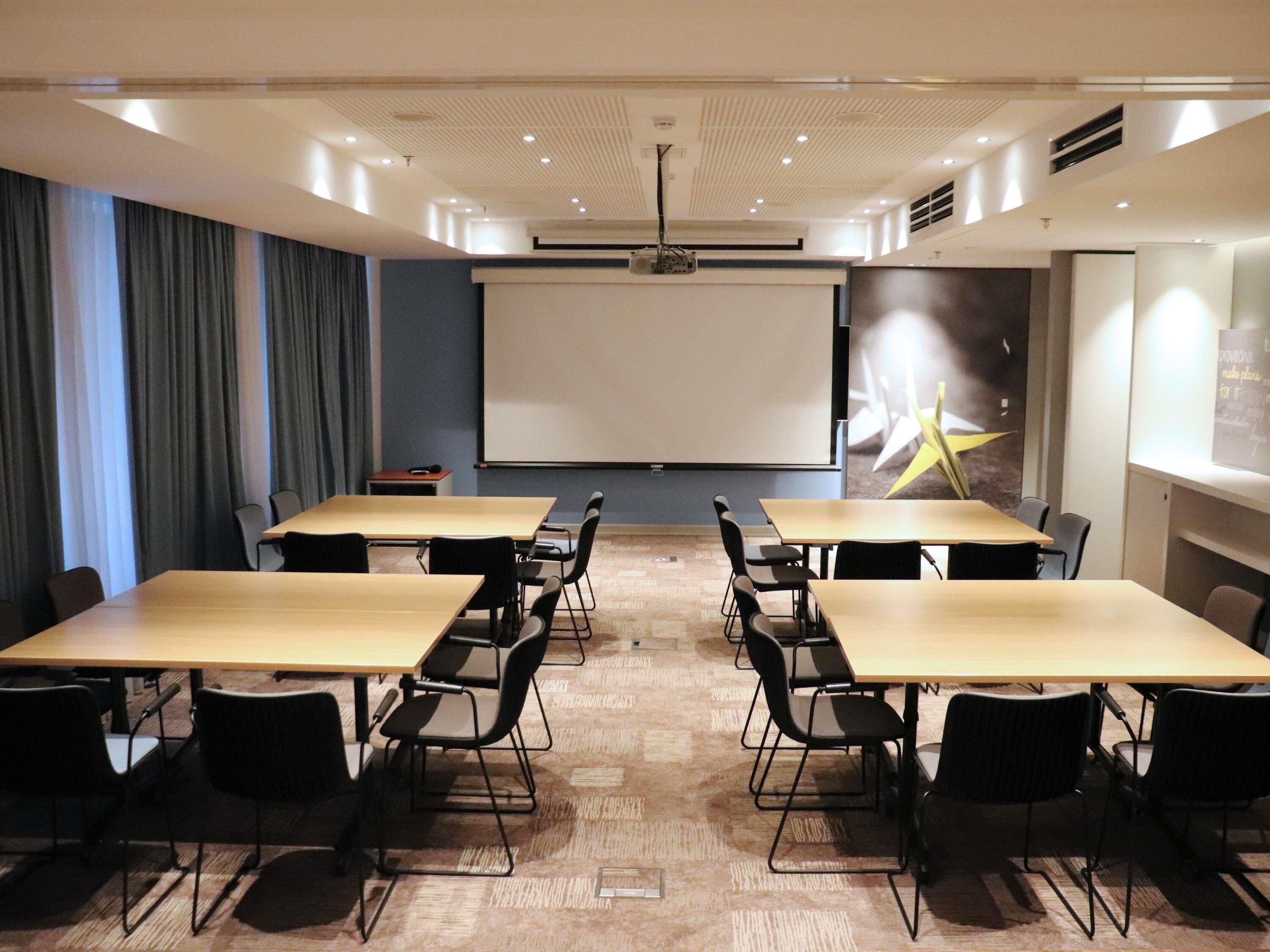 A conference room with a projector screen, tables, and chairs.