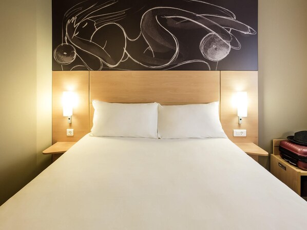 Une chambre d’hôtel avec un grand lit, deux lampes de chevet, une tête de lit en bois et une œuvre d’art décorative accrochée au mur au-dessus du lit.