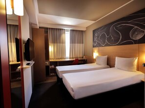 Habitación de hotel con dos camas, un escritorio con una silla, un televisor y un cuadro abstracto grande en la pared.