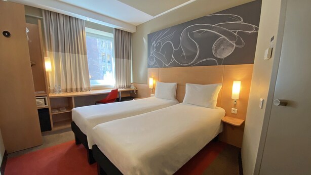 A hotel room with two beds, a desk, a chair, a window with curtains, and a wall with a chalkboard drawing. - ibis Yerevan Center (Yerevan)