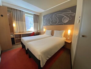 A hotel room with two beds, a desk, a chair, a window with curtains, and a wall with a chalkboard drawing. - ibis Yerevan Center (Yerevan)