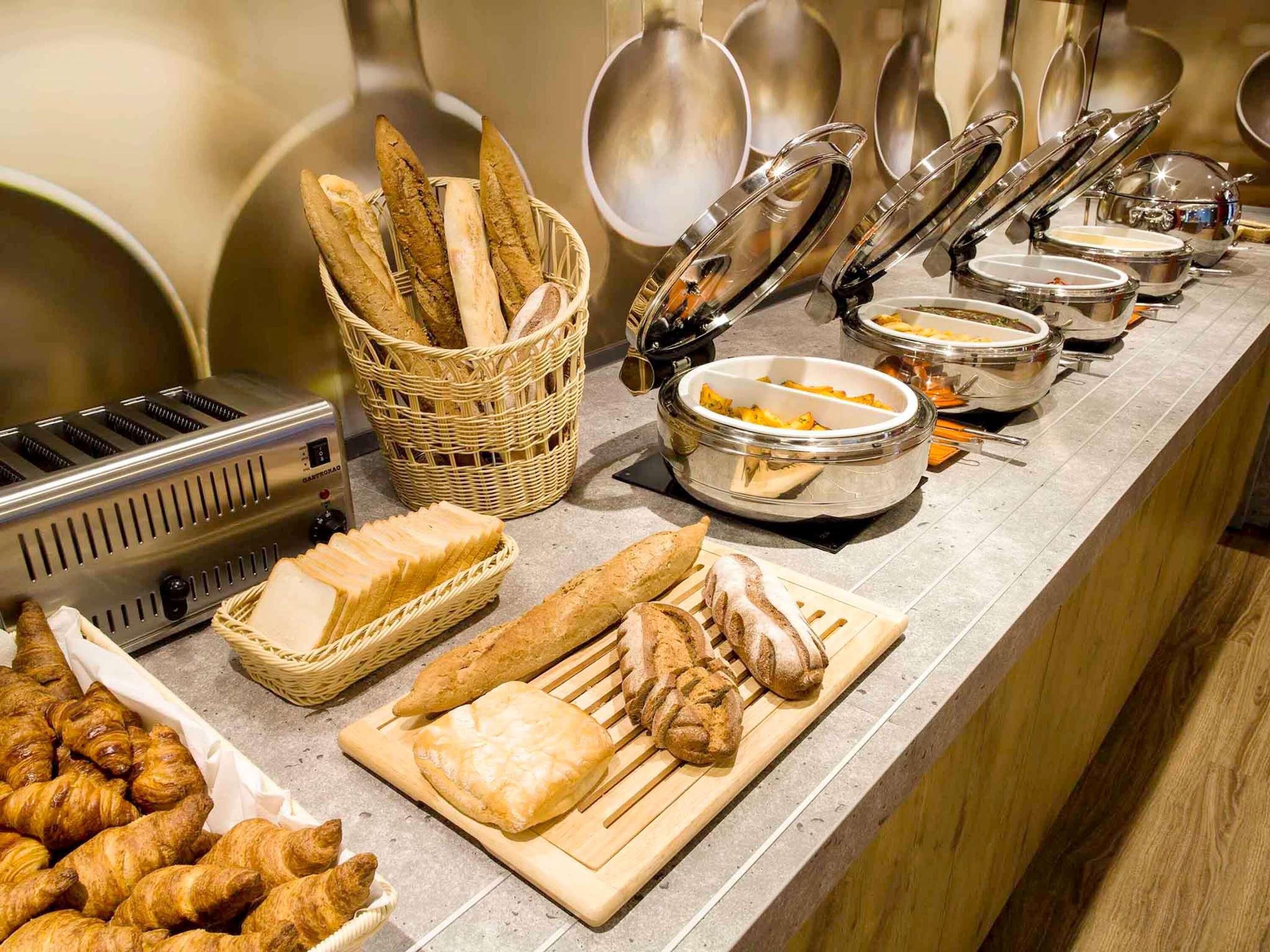A buffet with various breads, pastries, and hot dishes.