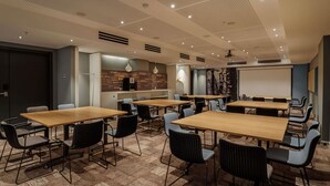 Un salón de conferencias con varias mesas y sillas, una pantalla de proyector y una pared con mensajes inspiradores.