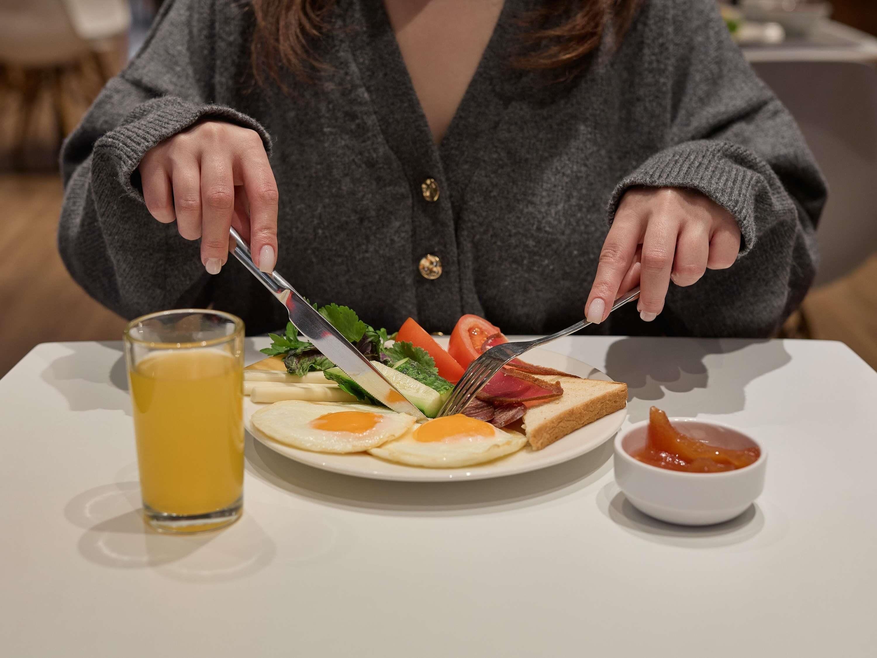 A breakfast plate with eggs, bacon, vegetables, and toast, a glass of orange juice, and a small bowl of jam.