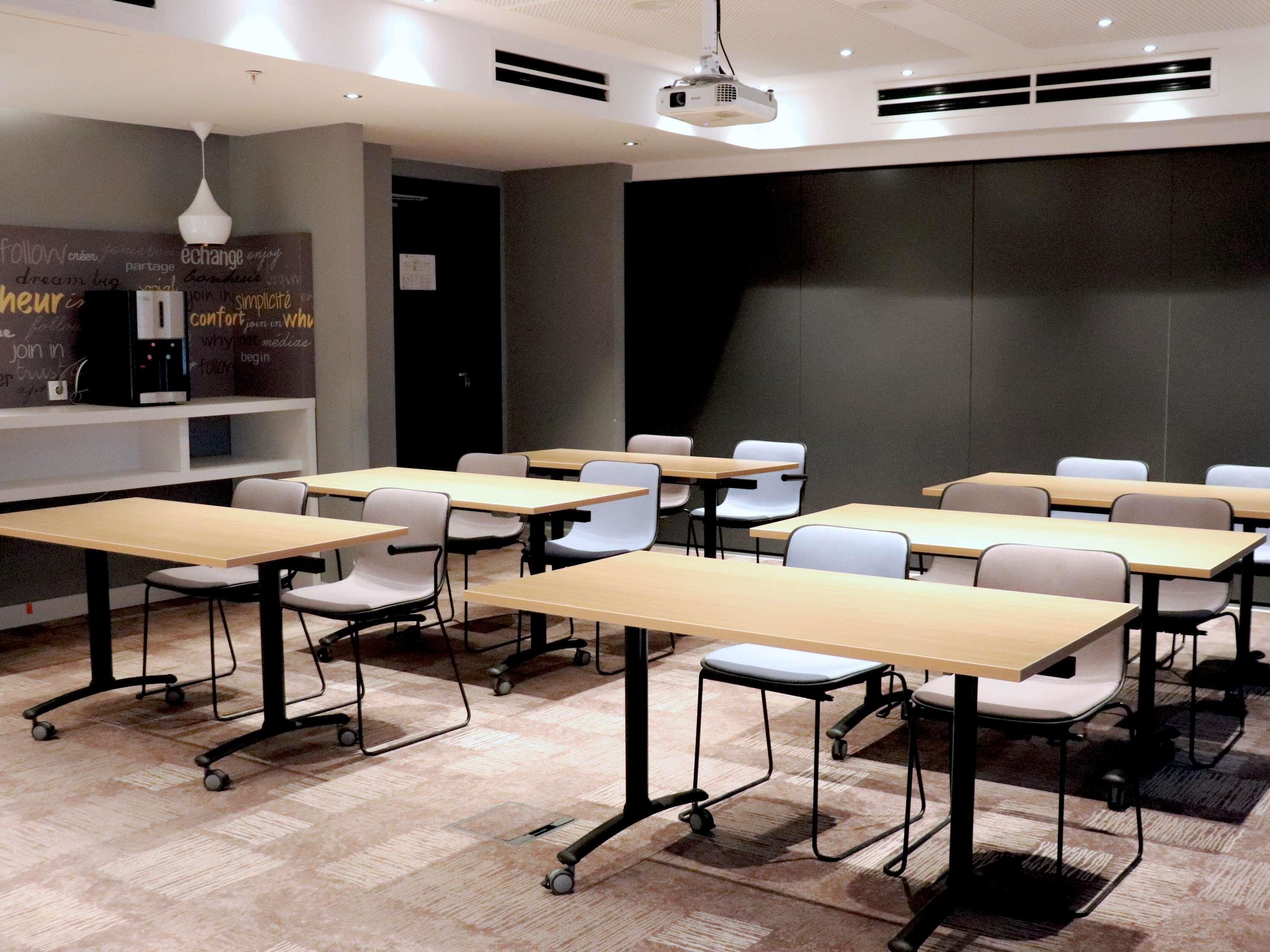 A conference room with multiple tables and chairs, a projector, and a wall with motivational words.