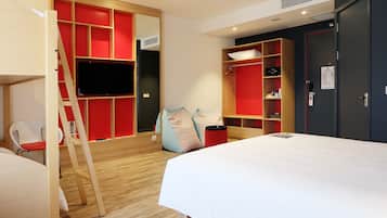 A modern hotel room with a bed, a TV mounted on a red wall, a wardrobe, and a wooden ladder.