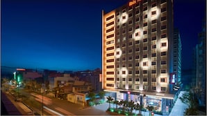 A modern hotel with a prominent 'ibis Hotel' sign, featuring a multi-story structure with evenly spaced windows and a well-lit facade. - ibis Saigon Airport (Ho Chi Minh City)
