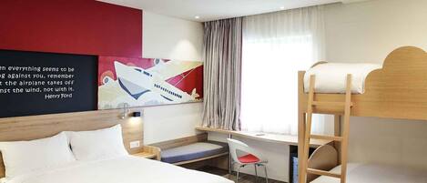 A hotel room with a bunk bed, a desk, a chair, and a bed.