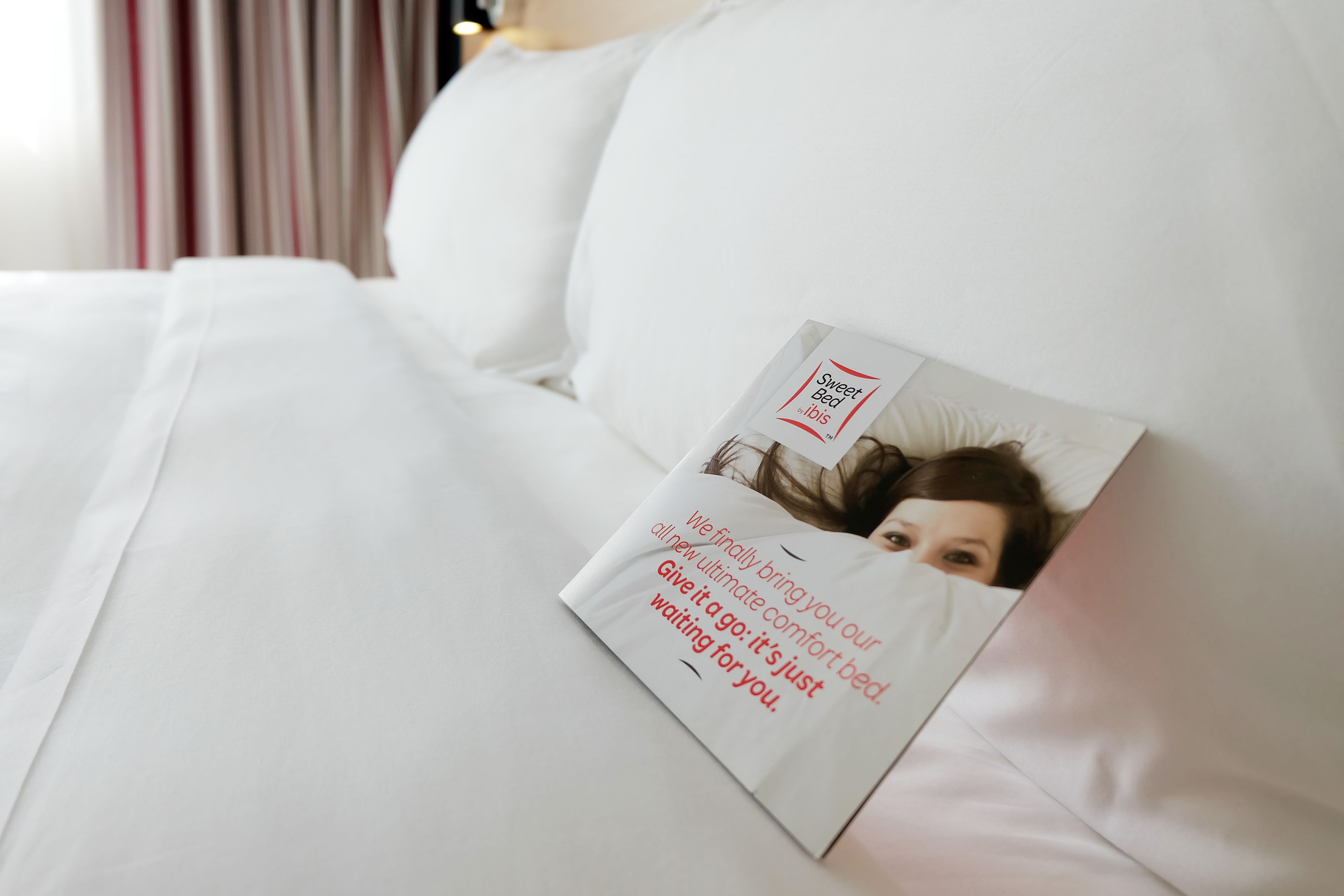 A white bed with a pillow that has a printed message.