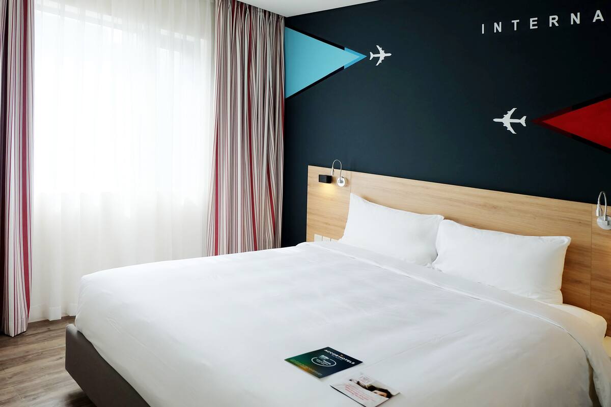 Habitación de hotel con una cama grande, cabecera de madera y una pared decorada con motivos aeronáuticos.