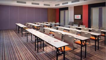 A conference room with multiple tables and chairs, a television screen, and a patterned carpet.