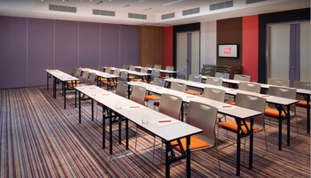 A conference room with multiple tables and chairs, a television screen, and a patterned carpet.