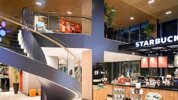 A modern interior with a Starbucks coffee shop, a curved staircase, and a seating area with orange stools.
