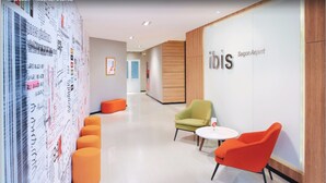 A modern hotel lobby with a seating area, a wall with text and graphics, and a sign for 'ibis Saigon Airport'. - ibis Saigon Airport (Ho Chi Minh City)