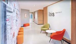 A modern hotel lobby with a seating area, a wall with text and graphics, and a sign for 'ibis Saigon Airport'.