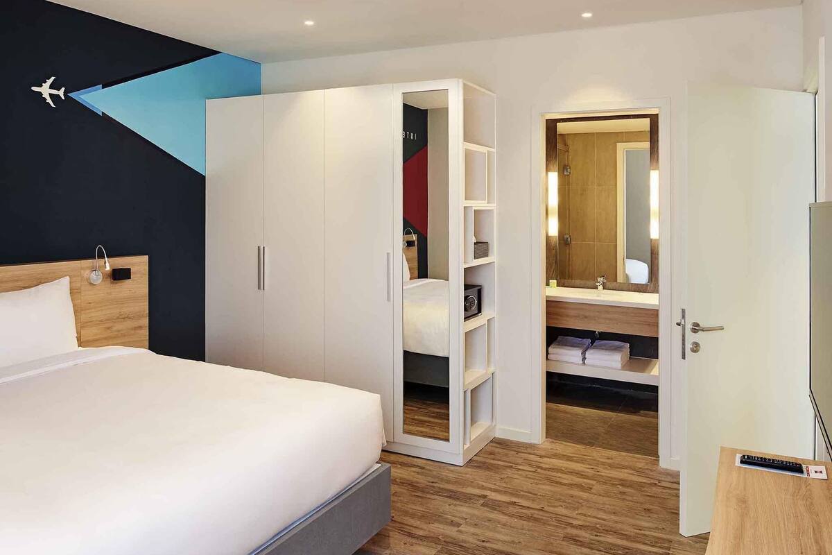 Habitación de hotel con cama, armario y baño con espejo.