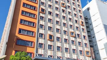 Un hotel de varios pisos con diseño moderno, que destaca por su fachada naranja y gris, amplios ventanales y una entrada porticada con palmeras.