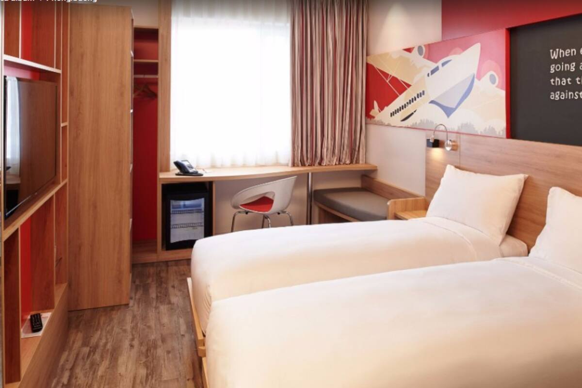 Una habitación de hotel con cama, escritorio, silla, armario y una pared con una cita motivacional.