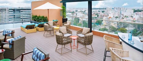 Eine Dachterrasse mit Korbmöbeln, einem Pool und Blick auf die Stadt.