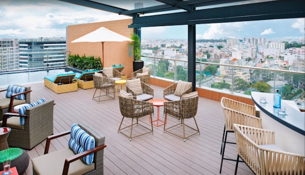 Una terraza en la azotea con mobiliario de mimbre, piscina y vistas a la ciudad.