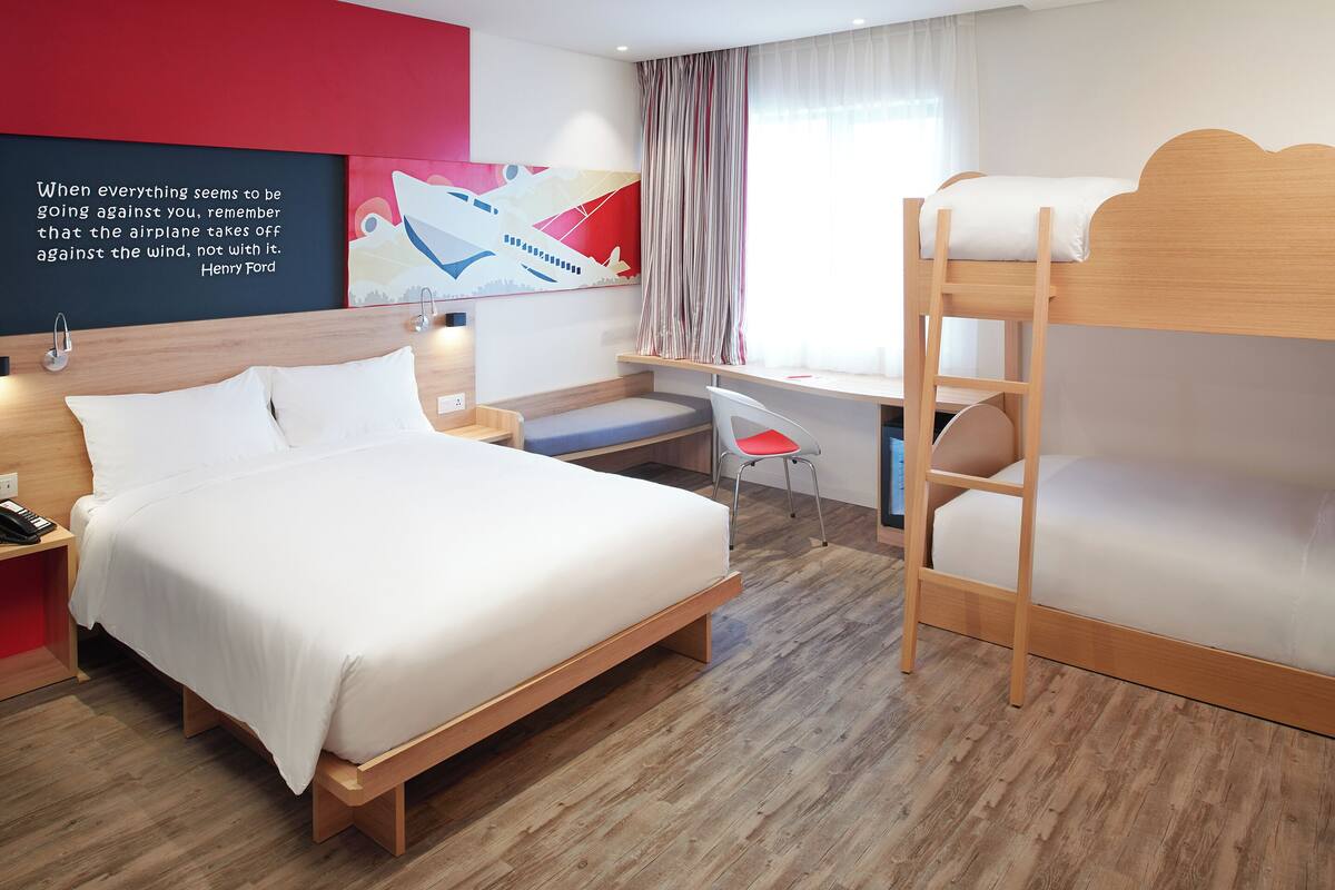 Una habitación de hotel moderna con una cama grande, un escritorio, una litera y una frase motivadora en la pared.