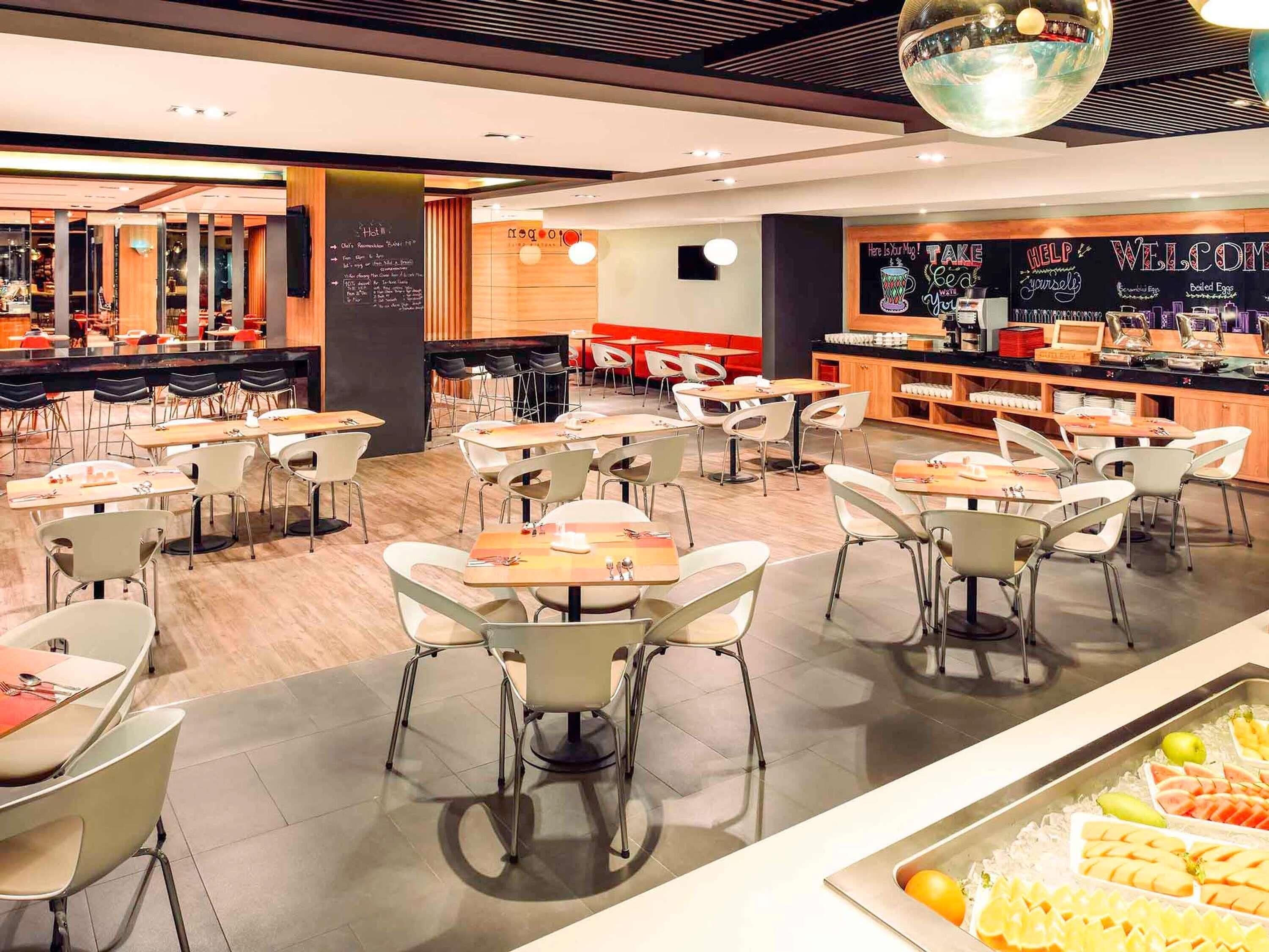 A modern restaurant with multiple tables and chairs, a bar area, and a chalkboard menu.