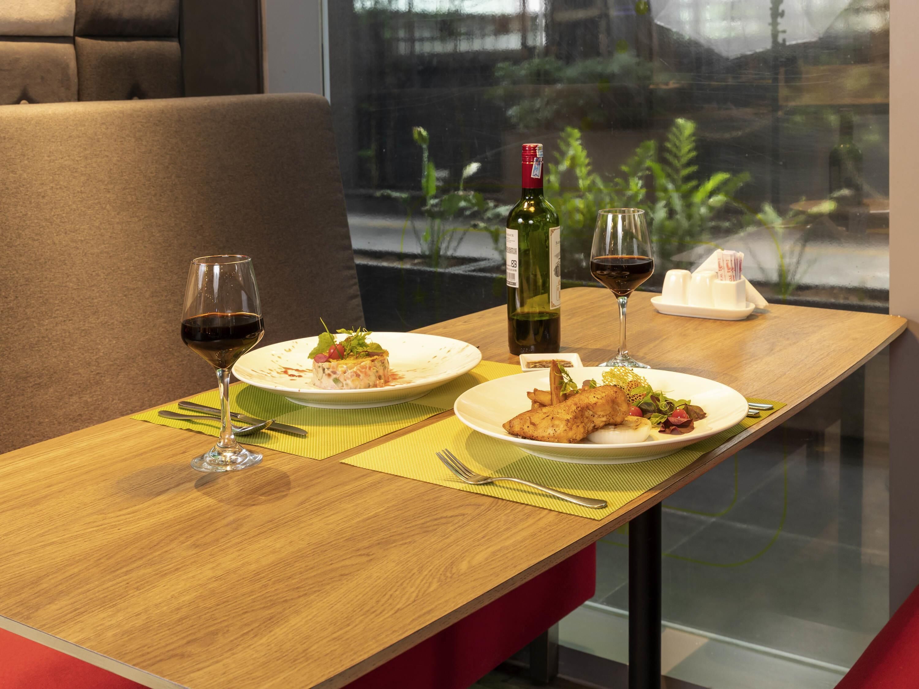 Una mesa de comedor con dos platos de comida, dos copas de vino y una botella de vino.