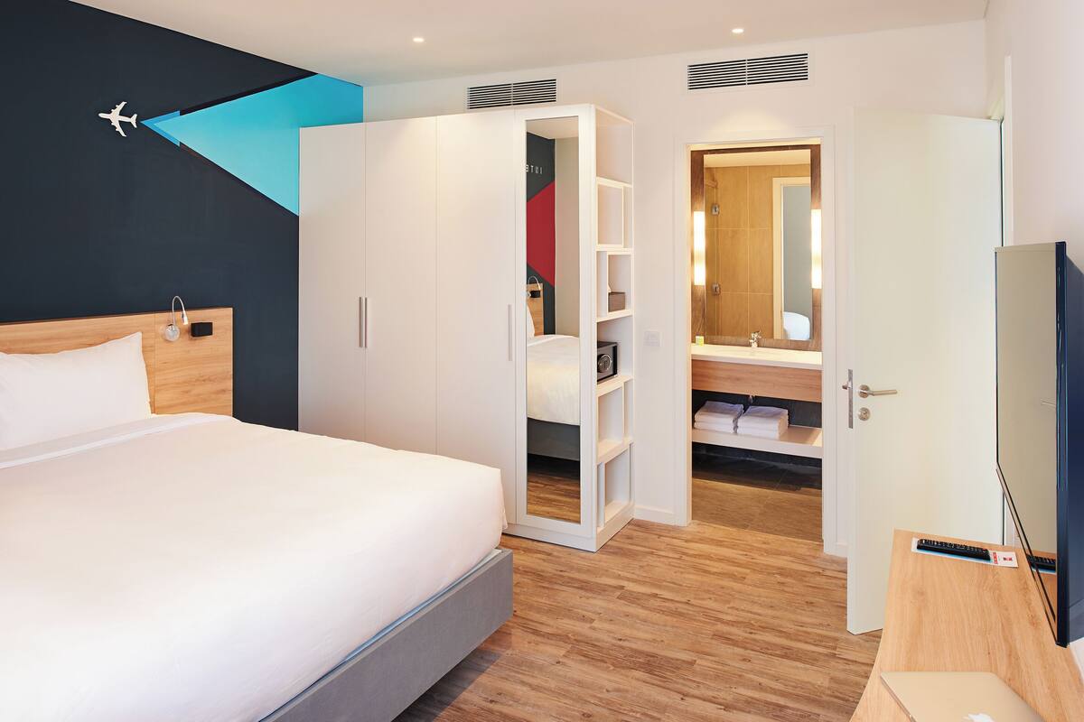 Habitación de hotel moderna con cama, armario, baño con espejo y televisión.