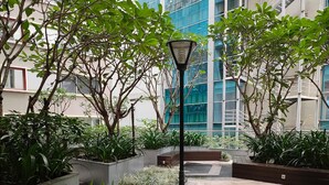 An outdoor courtyard with potted plants, a street lamp, and a modern building in the background. - ibis Saigon Airport (Ho Chi Minh City)
