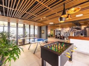 A modern indoor space with a foosball table, a bar area, and a view through large windows.